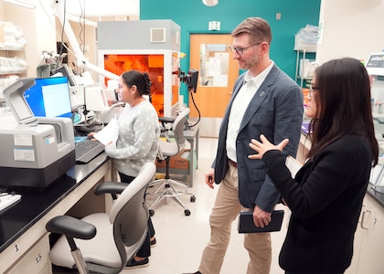 JOINT BASE SAN ANTONIO-FORT SAM HOUSTON (Dec. 8, 2025) Dr. Jeremy Pamplin, (center) program manager, Biological Technologies Office, Defense Advanced Research Projects Agency (DARPA), is briefed by research immunologist Dr. Dao Ho (right) and research scientist Phylisia Dimas, assigned to Naval Medical Research Unit (NAMRU) San Antonio on the specific methods by which NAMRU-SA assesses the viability and proliferation of living cells for DARPA’s Fieldable Solutions for Hemorrhage with bio-Artificial Resuscitation Products (FSHARP) program at the Battlefield Health & Trauma Research Institute. The FSHARP program works to develop a deployable, shelf-stable, universal whole blood substitute as a hemorrhage countermeasure to sustain injured warfighters in austere, pre-hospital settings. NAMRU San Antonio, part of Navy Medicine Research & Development, works alongside research partners in the civilian sphere, academia, industry, and other government agencies to drive support of the Department of War’s objectives for a lethal fighting force and ensures U.S. service members have access to the latest scientific advances. NAMRU San Antonio conducts gap-driven combat casualty care, craniofacial, and directed energy research in support of Navy, Marine Corps and joint U.S. warfighter health readiness and lethality while engaged in routine and expeditionary operations. (U.S. Navy photo by Burrell Parmer/Released)