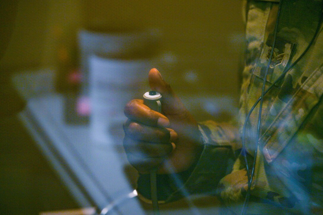 A service member's thumb rests over a button