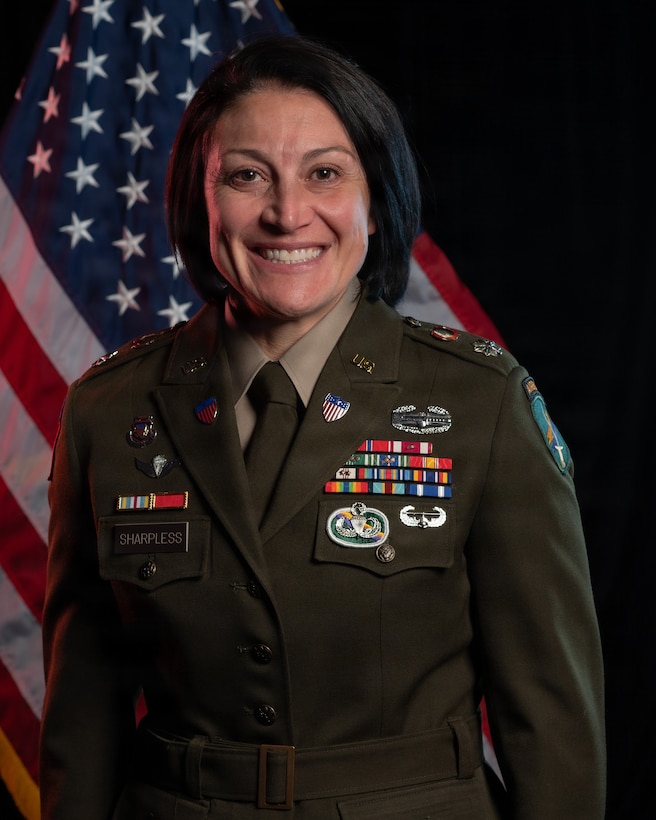 Woman wearing U.S. Army uniform standing in front of two flags.