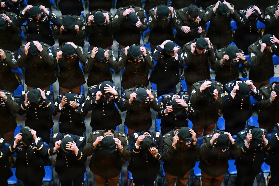 Dozens of soldiers stand in formation during a ceremony while adjusting their green berets as seen from above.