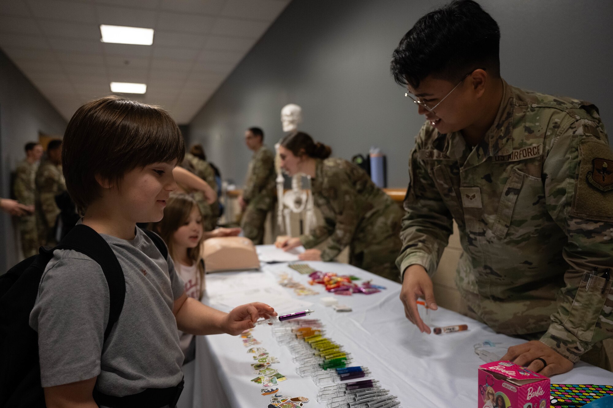 U.S. Air Force Senior Airman Michael Keith San Jose, 47th Healthcare Operations Squadron medical laboratory technician, hands out pens to a Junior Deployment participant during a Junior Deployment event at Laughlin Air Force Base, Texas, Nov. 21, 2025. San Jose assisted participants by joining a simulated pre-deployment function line. (U.S. Air Force photo by Airman 1st Class Darryl Keith)