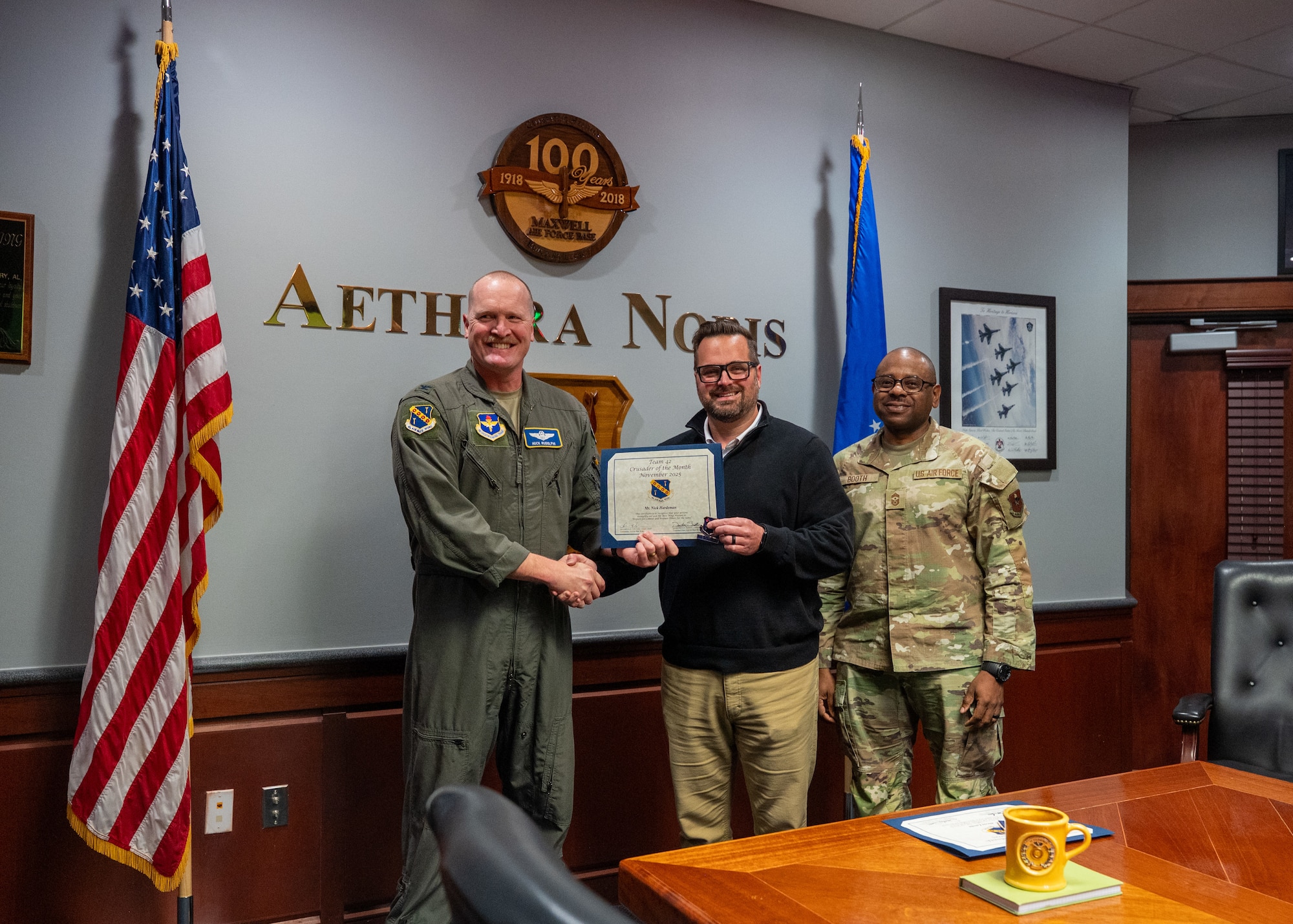 U.S Air Force Col. Adam Rudolphi, 42d Air Base Wing deputy commander, and Chief Master Sgt. Demetrius Booth, 42d ABW command chief, present the Crusader of the Month award for November to Ryan Hardeman, Maxwell Air Force base, Ala. Dec. 11, 2025.