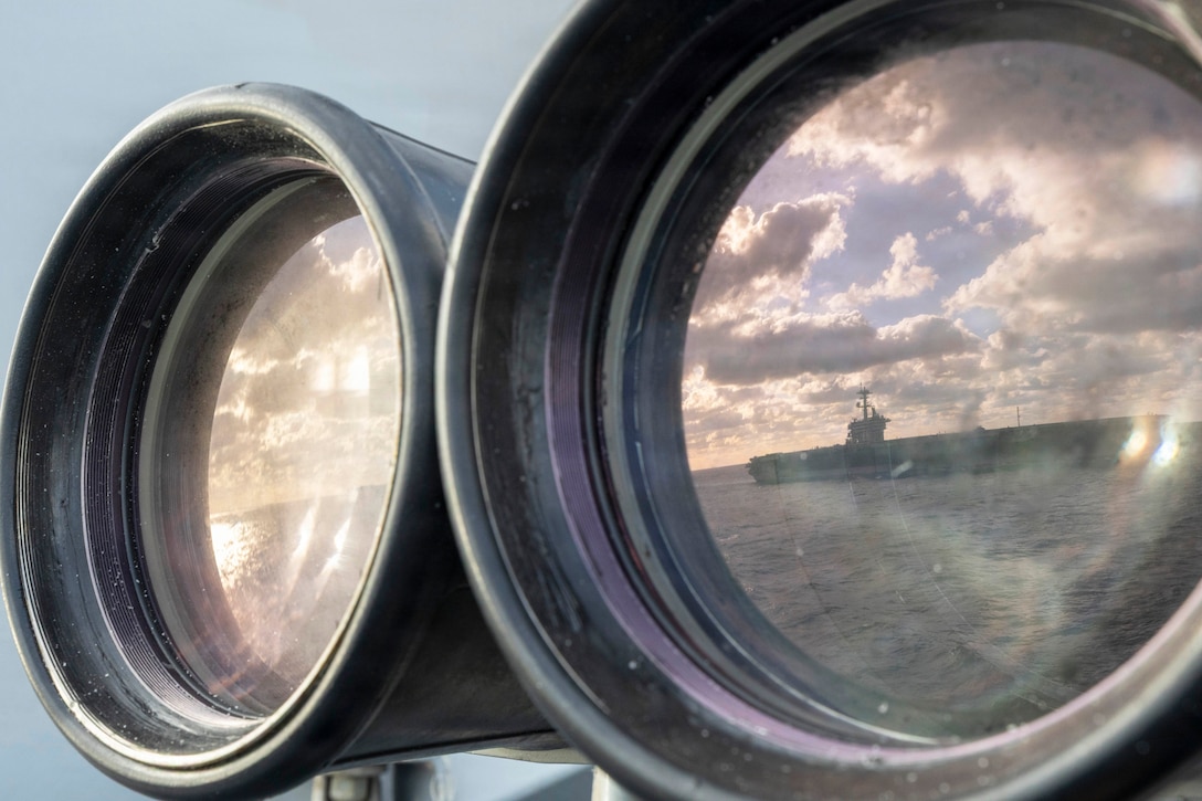A ship transits a body of water as seen through large binoculars attached to another ship.