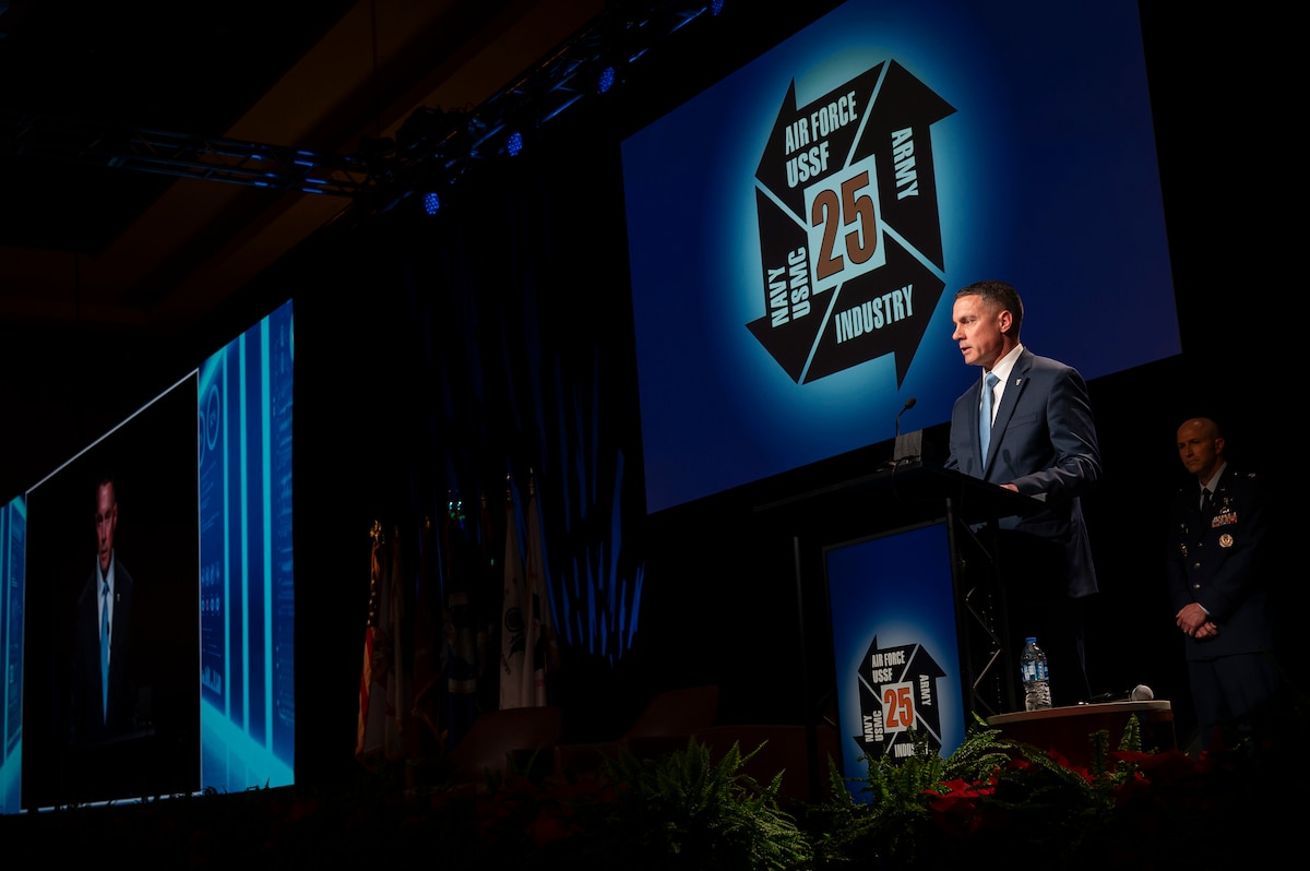 Man in suit stands on a stage behind podium and gives a speech.