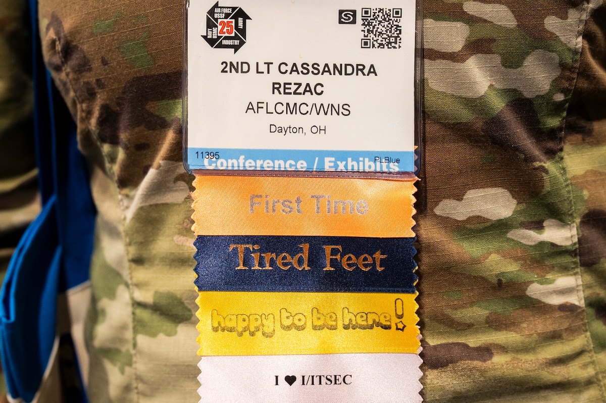 Image shows a conference badge with many ribbons that say First Timer, Tired Feet, Happy To Be Here.