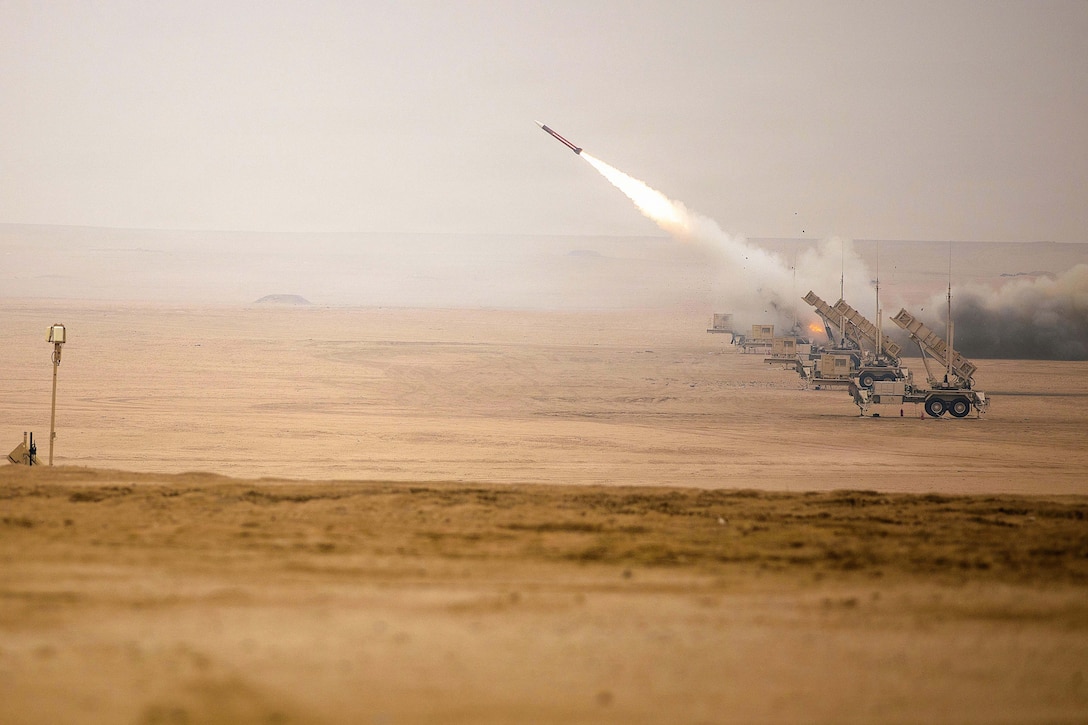 A missile launches from a desert-like area into a hazy sky, leaving behind clouds of smoke.