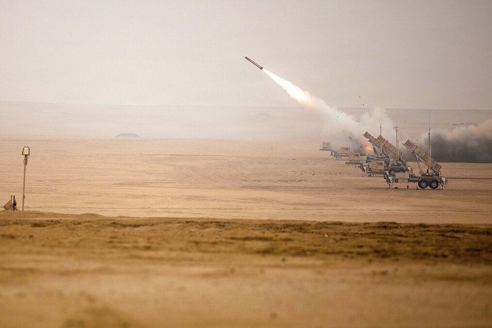 A missile launches from a desert-like area into a hazy sky, leaving behind clouds of smoke.