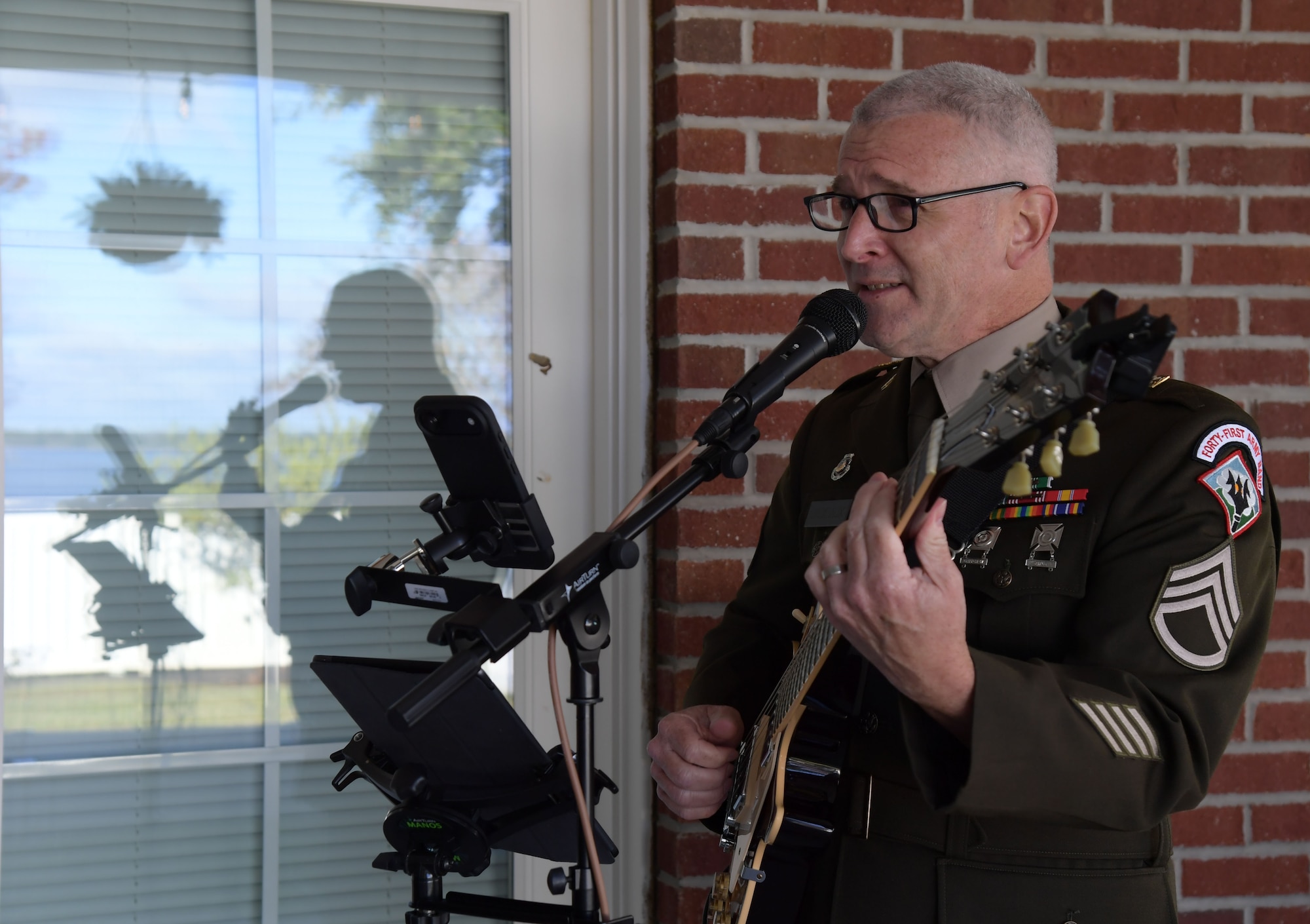 A man in military uniform plays a guitar while singing.