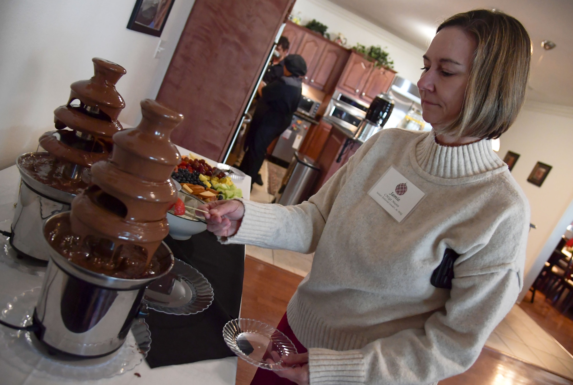 A woman dips a strawberry in chocolate.