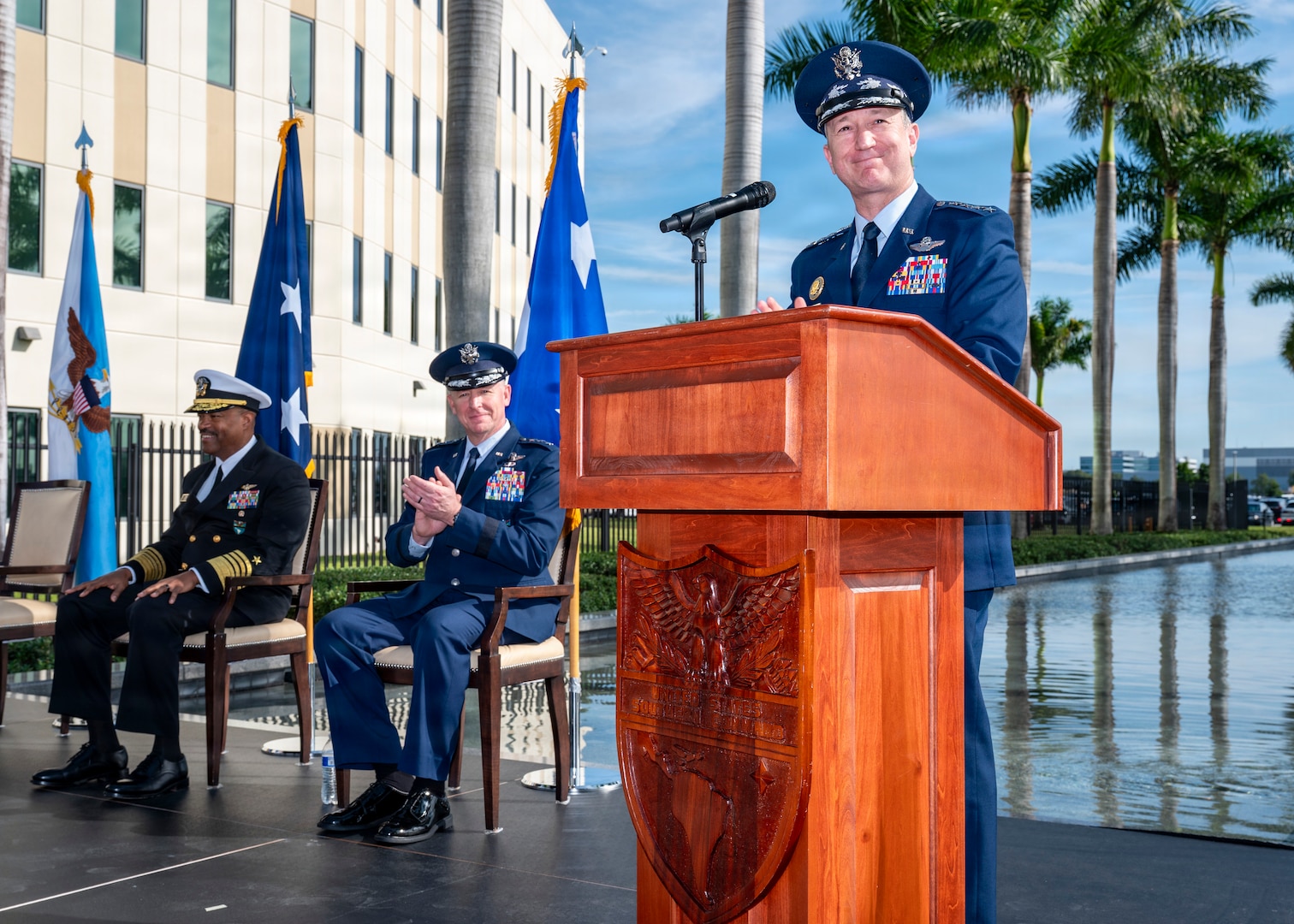 A man in a blue military unform address a large crowd from behind a podium.