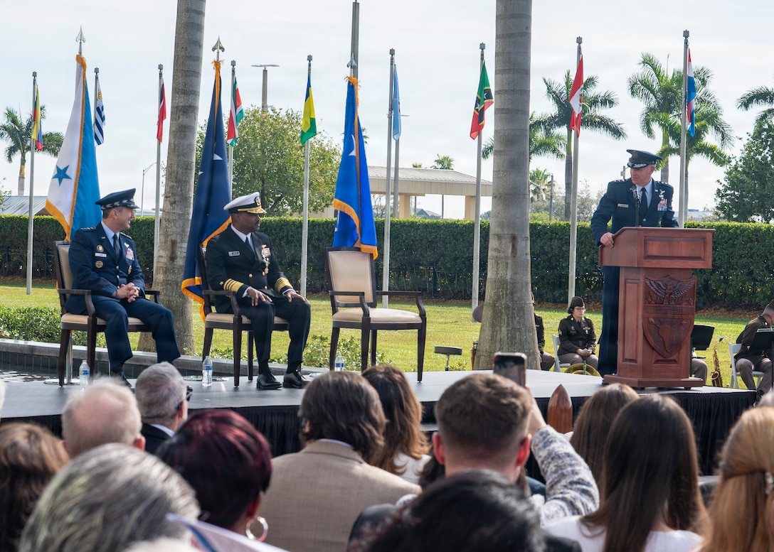A man in a blue military unform address a large crowd from behind a podium.