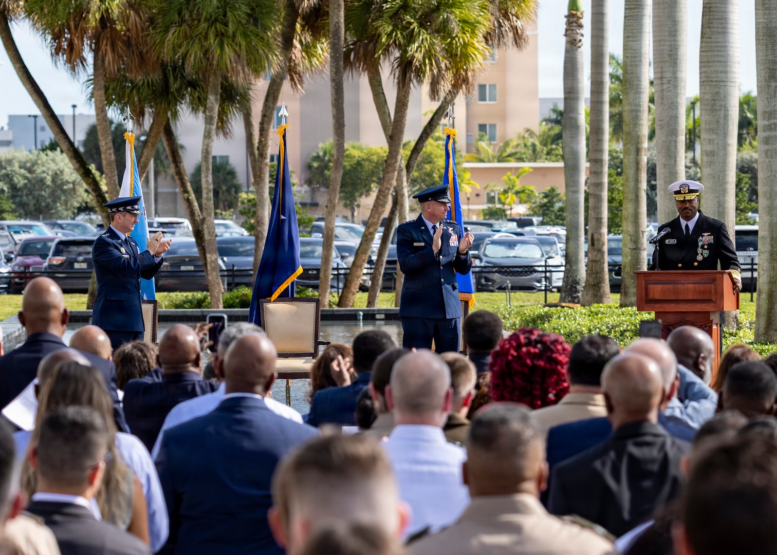 A man in a black military unform address a large crowd from behind a podium.