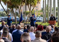 A man in a black military unform address a large crowd from behind a podium.