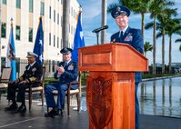A man in a blue military unform address a large crowd from behind a podium.