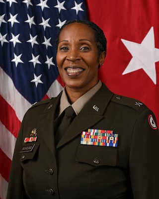 woman wearing U.S. Army uniform standing in front of two flags.