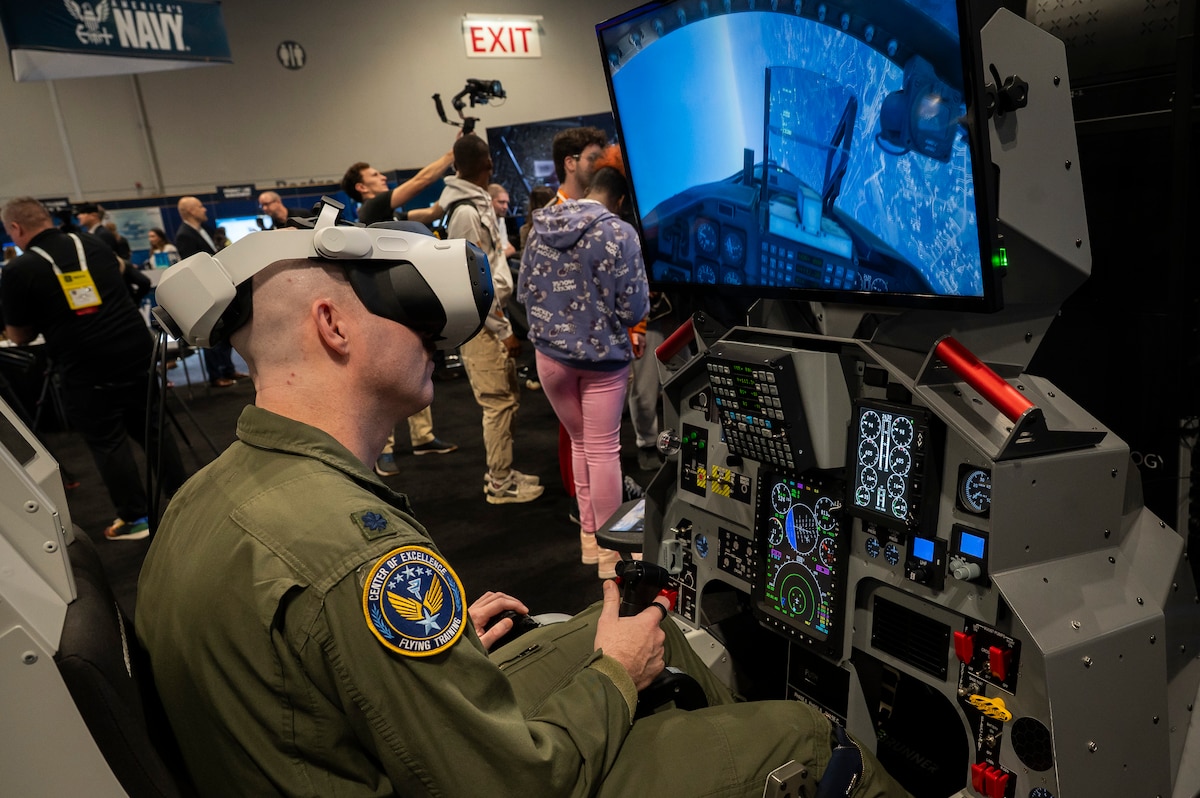 Man in Air Force jumpsuit uses a flight simulator and V/R googles.