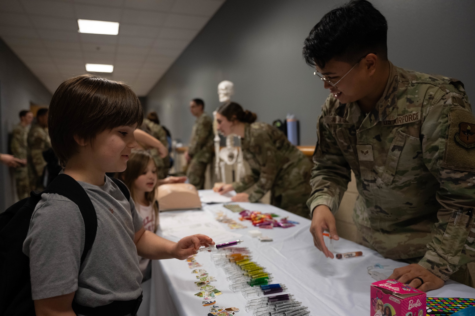 U.S. Air Force Senior Airman Michael Keith San Jose, 47th Healthcare Operations Squadron medical laboratory technician, hands out pens to a Junior Deployment participant during a Junior Deployment event at Laughlin Air Force Base, Texas, Nov. 21, 2025. San Jose assisted participants by joining a simulated pre-deployment function line. (U.S. Air Force photo by Airman 1st Class Darryl Keith)