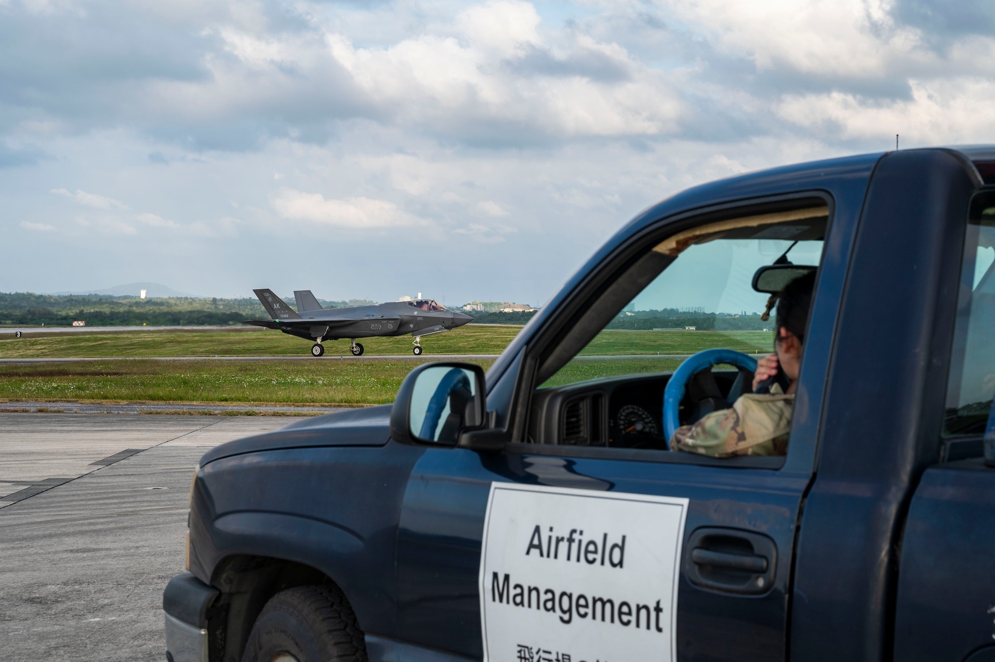 U.S. Air Force Senior Airman Dana Nguyen, 18th Operations Support Squadron airfield management shift lead, observes an F-35 Lightning II assigned to the 356th Expeditionary Fighter Squadron, deployed to Kadena Air Base, taxiing on the flight line at Kadena Air Base, Japan, Dec. 11, 2025.