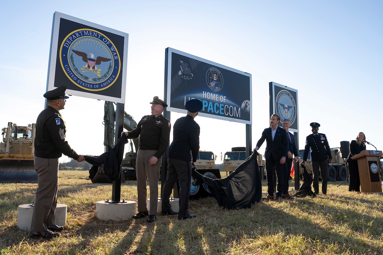 The secretary of war alongside Space Force and Army leadership unveil signs in a field.