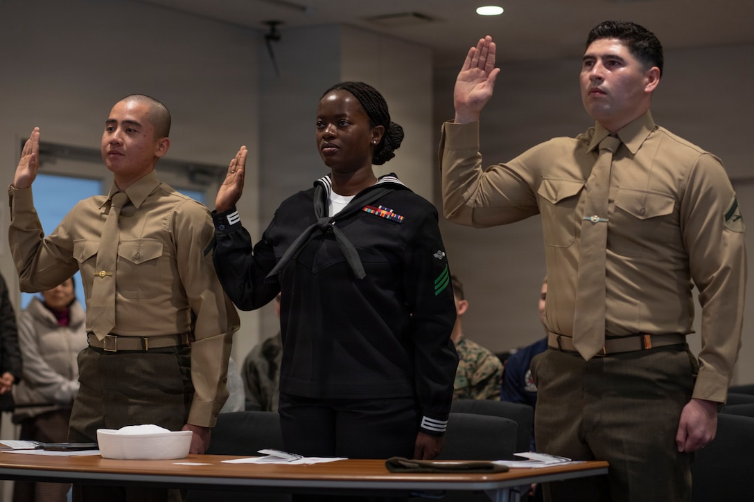 U.S. Marine Corps Lance Cpl. Nguyen Vu, left, a power line mechanic with Marine Aerial Refueler Transport Squadron (VMGR) 152, Marine Aircraft Group 12, 1st Marine Aircraft Wing, U.S. Navy Aviation Machinist’s Mate Adama Ceesay, center, with Headquarters and Headquarters Squadron, Marine Corps Air Station Iwakuni,  and U.S. Marine Corps Lance Cpl. Kevin Barrios Palafox, right, a fixed wing aircraft safety mechanic with VMGR-152, MAG-12, 1st MAW, raise their right hands for the oath of allegiance during a naturalization ceremony at MCAS Iwakuni, Japan, Nov. 26, 2025. The naturalization ceremony was held to acknowledge military service members’ accomplishment of becoming United States citizens. (U.S. Marine Corps photo by Lance Cpl. Tyler Bassett)