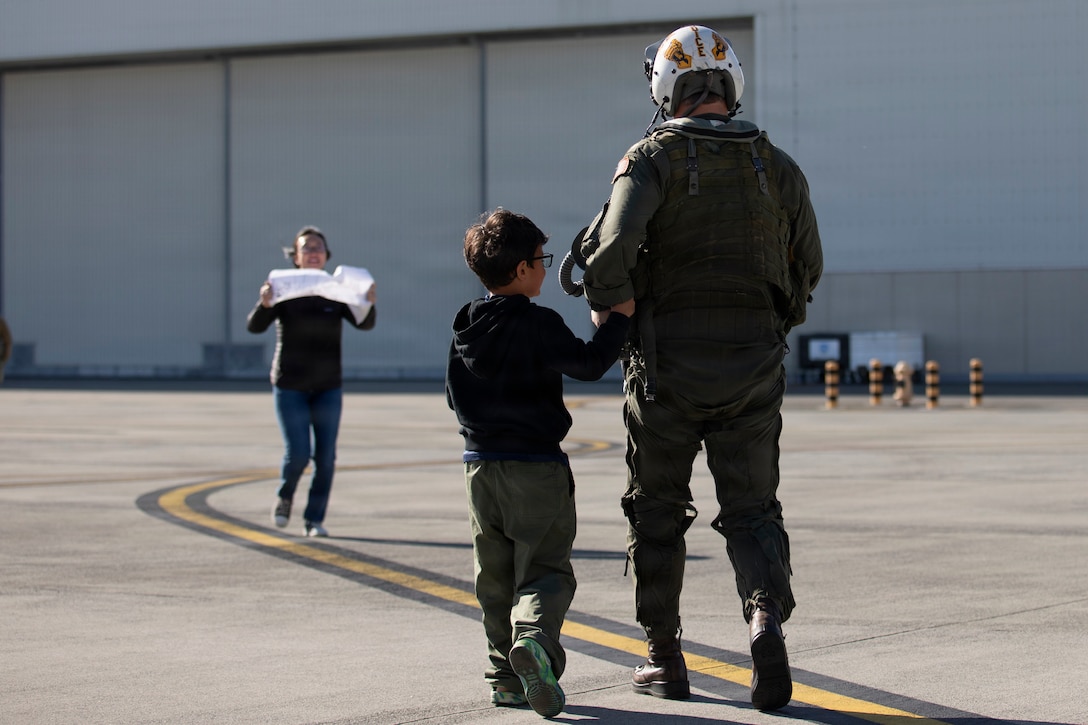 U.S. Navy LCDR Robert Ward, a pilot with Strike Fighter Squadron (VFA) 27, Carrier Air Wing (CVW) 5, greets his family at Marine Corps Air Station Iwakuni, Japan, Dec. 3, 2025. CVW-5 aircraft and personnel return from being forward-deployed on the Nimitz-class aircraft carrier USS George Washington (CVN-73) which provided air superiority and all-weather offensive air-to-surface attack capabilities, to maintain a free and open Indo-Pacific. (U.S. Marine Corps photos by Lance Cpl. Tyler Bassett)
