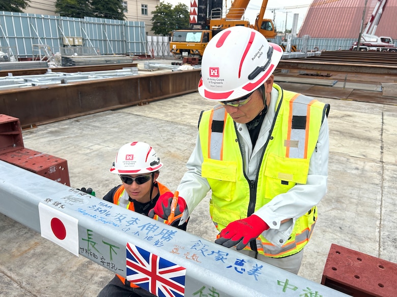 U.S. Army Corps of Engineers – Japan Engineer District (USACE JED) Yokota Resident Office team members, Rion Ogawa, an engineering technician (left), and Tatsuya Kokubu, a construction representative, sign a structural beam during a Topping Off ceremony on October 3rd, 2025. The structural beam was the last to be placed in the Yokota Air Base’s currently undergoing construction Corrosion Control Hangar. During the ceremony, special thanks were provided to the intercultural team members involved in the project, and how projects designed and constructed by JED often bring together individuals from a wide range of professional and international backgrounds. Courtesy photo provided by Gilbane Japan.