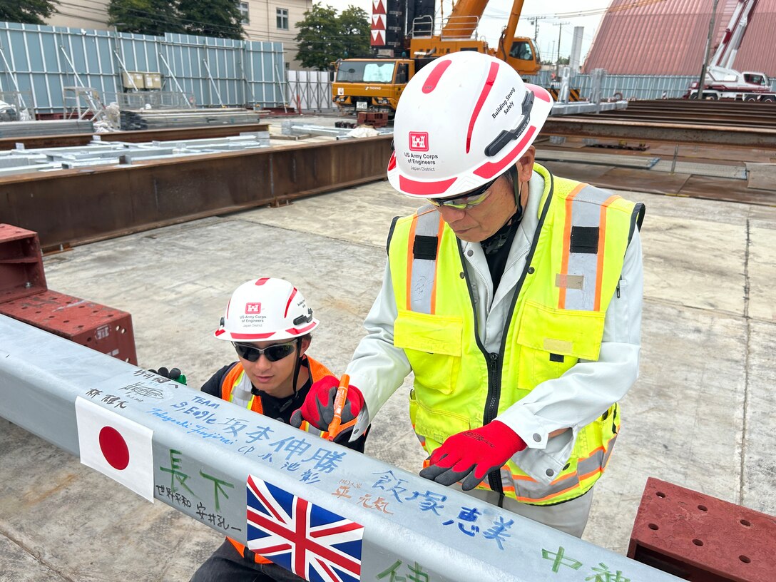 U.S. Army Corps of Engineers – Japan Engineer District (USACE JED) Yokota Resident Office team members, Rion Ogawa, an engineering technician (left), and Tatsuya Kokubu, a construction representative, sign a structural beam during a Topping Off ceremony on October 3rd, 2025. The structural beam was the last to be placed in the Yokota Air Base’s currently undergoing construction Corrosion Control Hangar. During the ceremony, special thanks were provided to the intercultural team members involved in the project, and how projects designed and constructed by JED often bring together individuals from a wide range of professional and international backgrounds. Courtesy photo provided by Gilbane Japan.