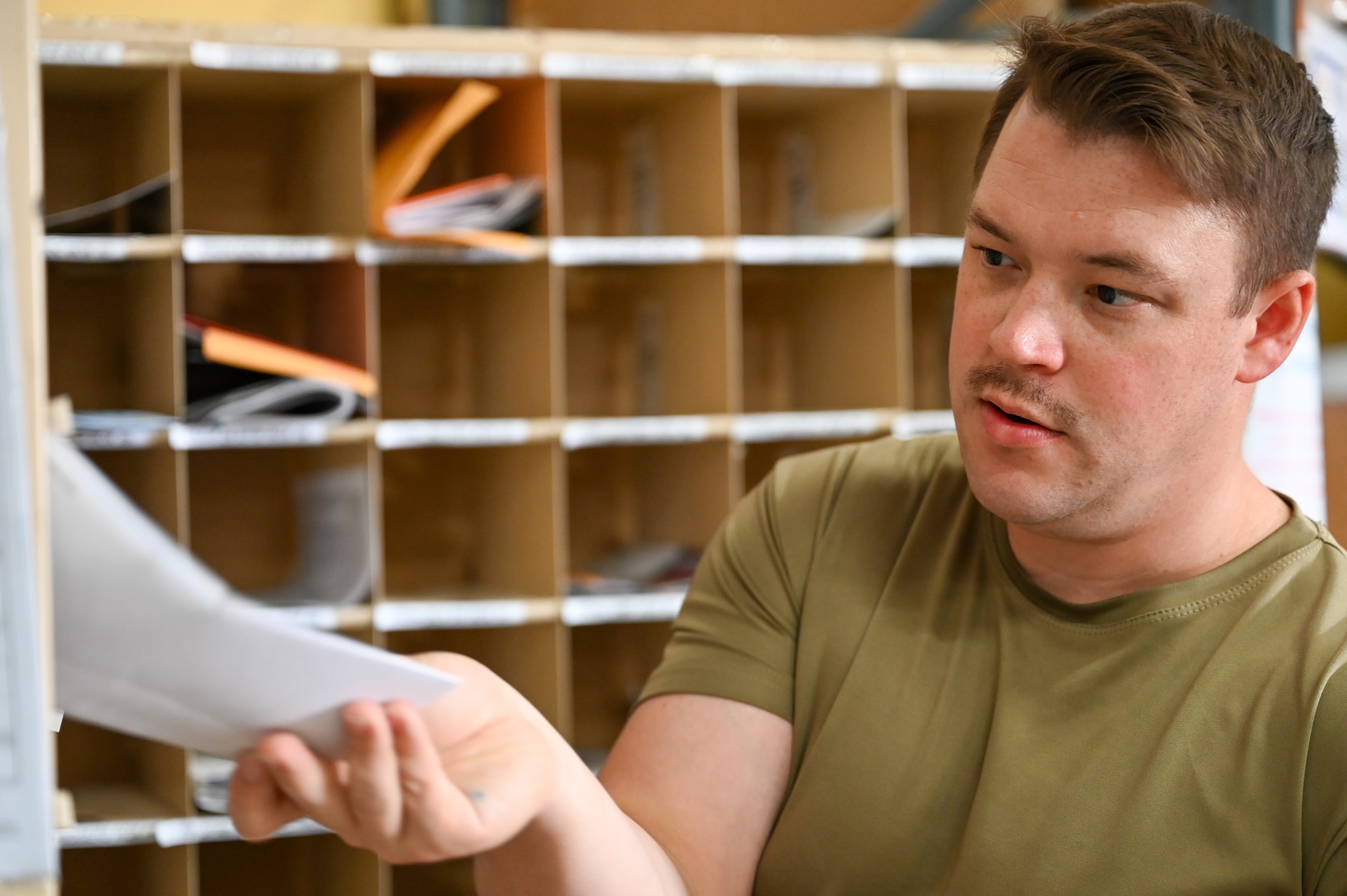 An Airman in a mail room slides an envelope into an out of frame mail cubby