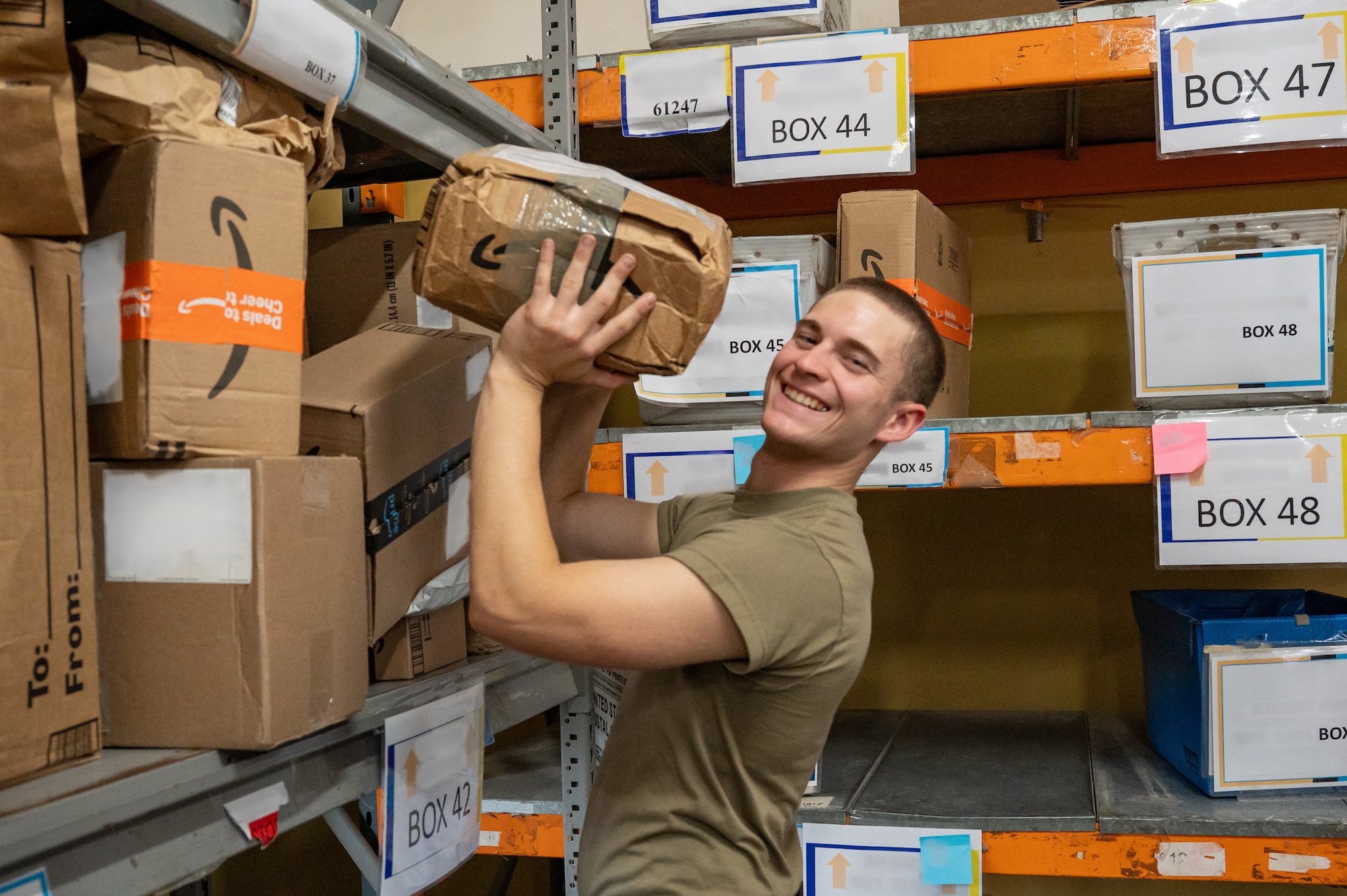 An Airman places a box on a shelf of other boxes while smiling