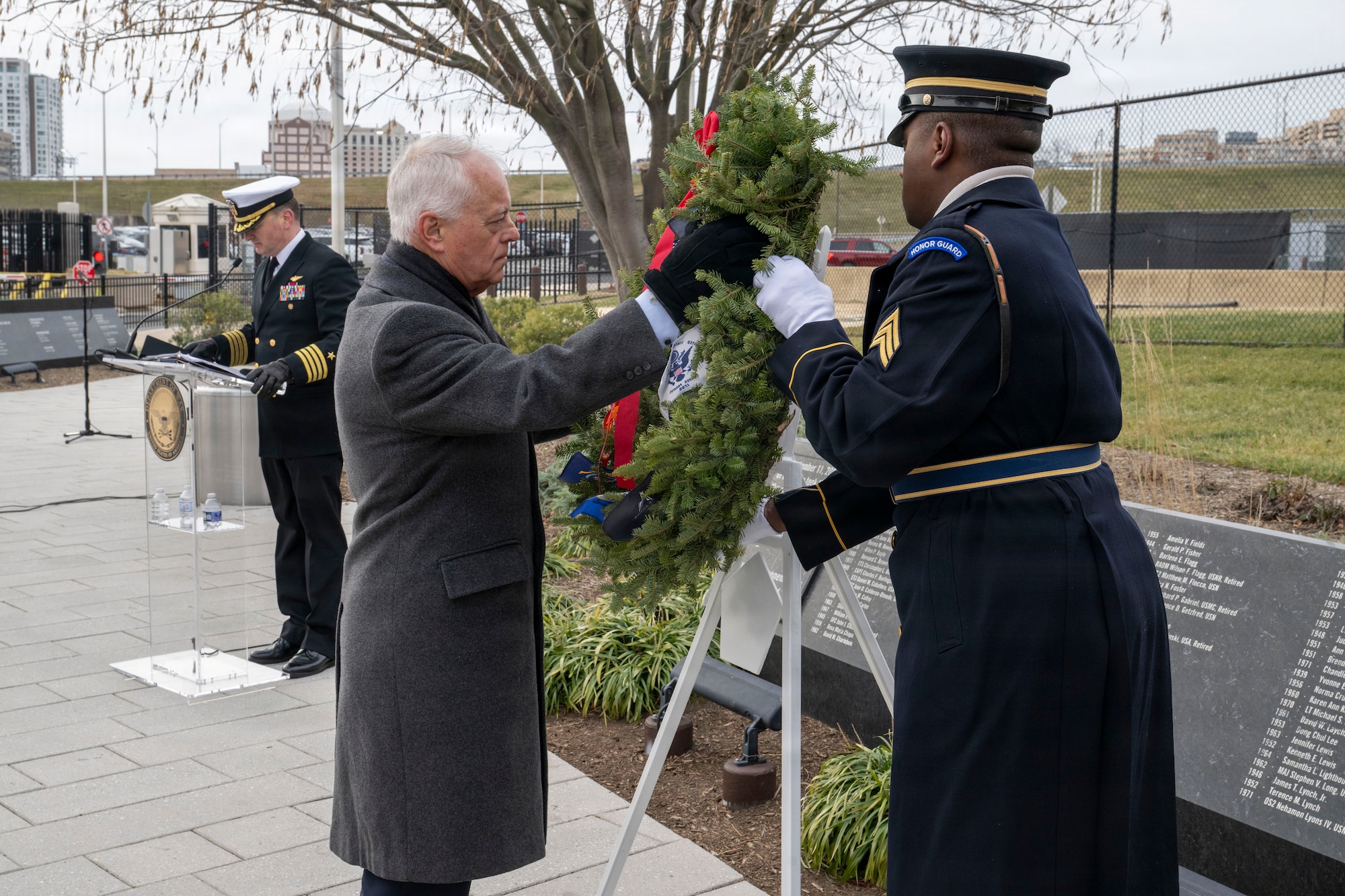 A man assists a service member in displaying a wreath on an easel outside.