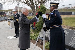 A man assists a service member in displaying a wreath on an easel outside.