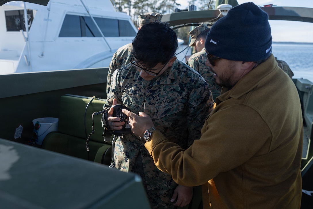 U.S. Marine Corps Cpl. Alexander Bribiezca, an engineer equipment mechanic with Maritime Distribution Platoon, 2nd Distribution Support Battalion, Combat Logistics Regiment 2, left, receives instruction from a U.S. Department of War contractor on a SEAFLIR 240-EP maritime surveillance sensor at Marine Corps Base Camp Lejeune, North Carolina, Dec. 10, 2025. 2nd Marine Logistics Group is working with the Marine Corps Warfighting Lab to experiment with the riverine assault support system for a more lethal, agile, and resilient capability while conducting expeditionary advanced base operations. Bribiezca is a native of Idaho. (U.S. Marine Corps photo by Sgt. Rafael Brambila-Pelayo)
