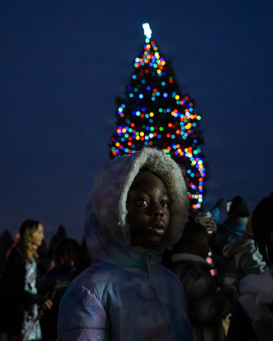 A child in the foreground looks off with a Christmas Tree behind them in the background