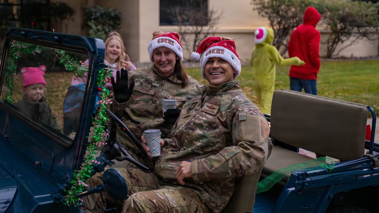 Two Airmen sit in a vehicle smiling at the camera