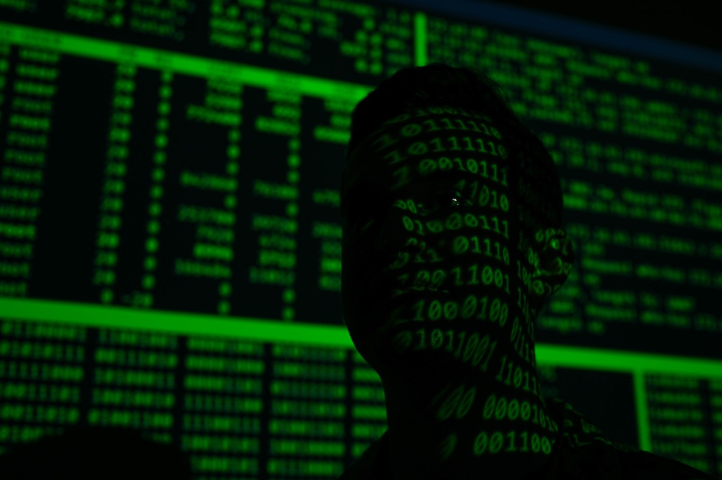 A silhouetted head is seen with green binary code displayed over their face, with green and black code displayed behind them.