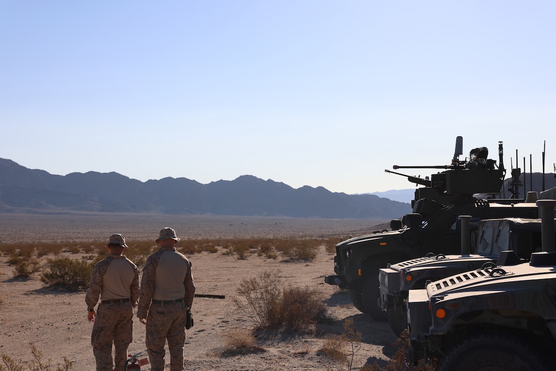 Two Marines walking towards the mountains in the sandy dessert of California with a MADIS system on the right.