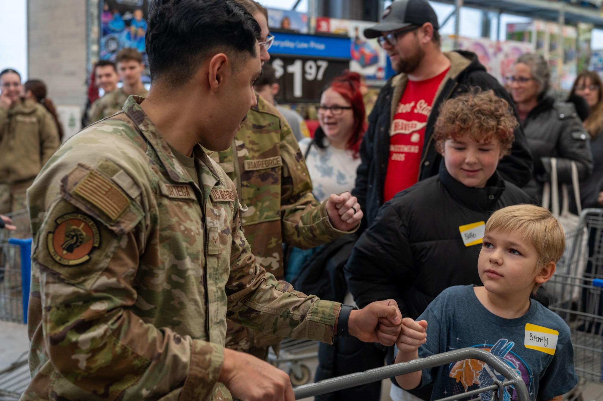 A U.S. Air Force Defender assigned to 791st Missile Security Forces Squadron gives a fist bump to a child during the Cops and Kids event at Walmart in Minot, North Dakota, Dec. 14, 2025. The event paired children with law enforcement officers and military personnel to shop for gifts, thereby strengthening community connections. (U.S. Air Force photo by Senior Airman Luis Gomez)