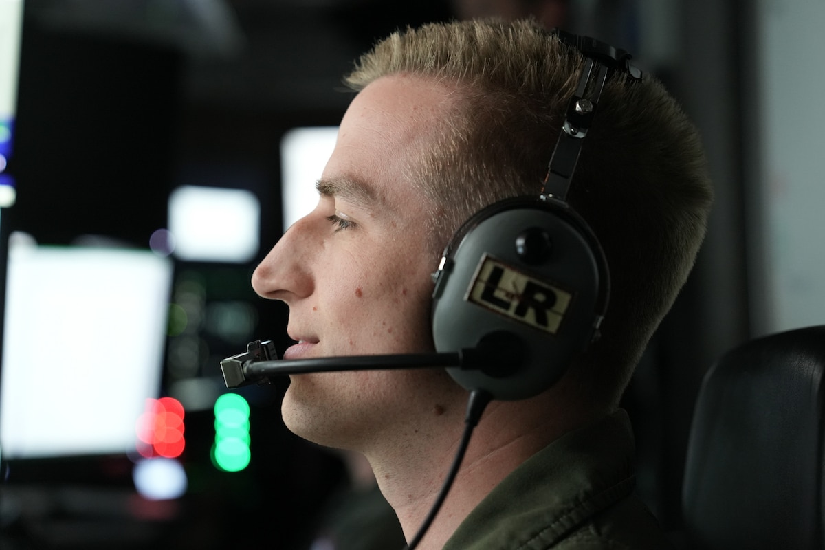 A man in a military uniform wearing headphones with "LR" on them.