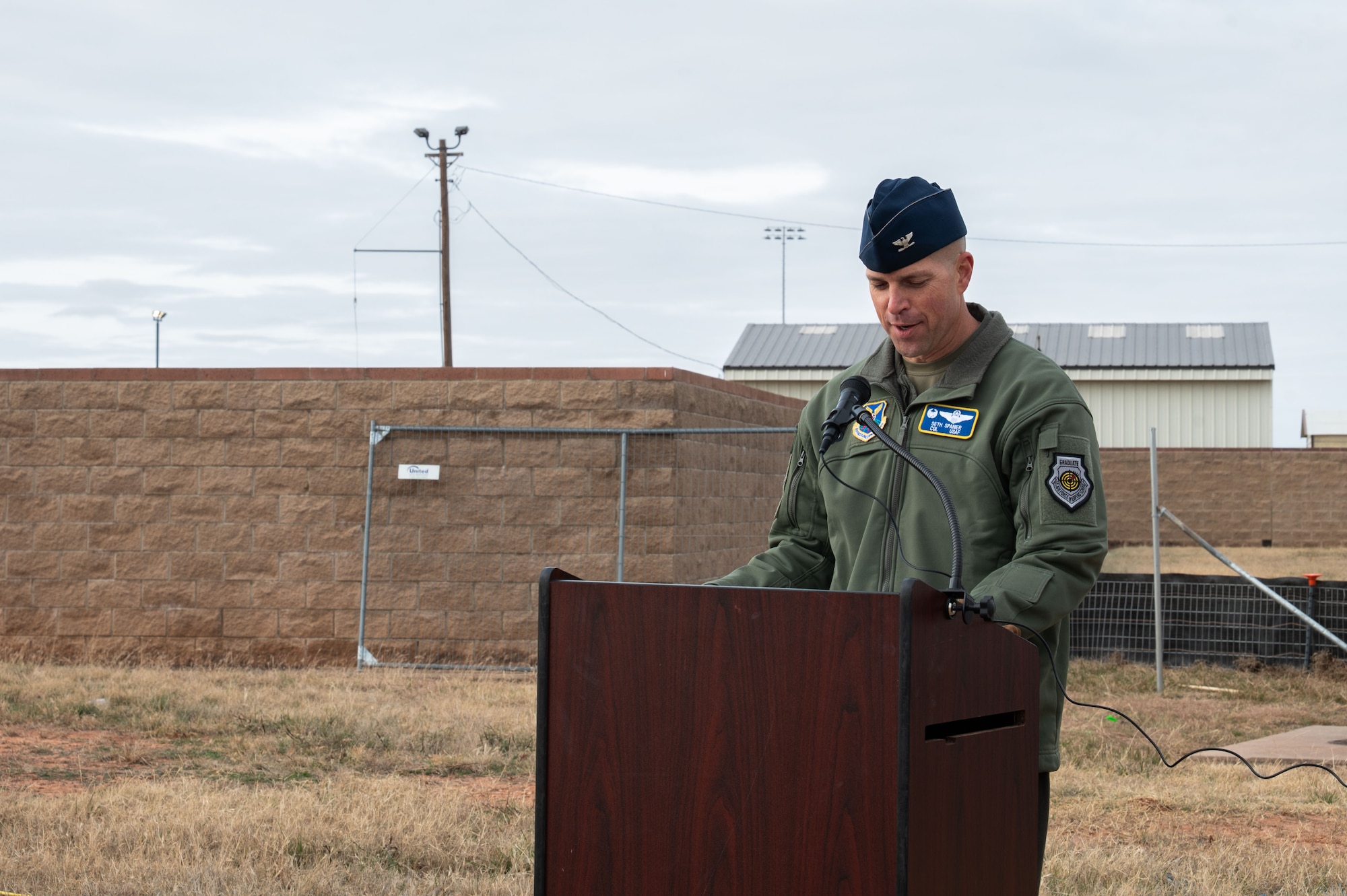 man stands behind a lectern outside speaking