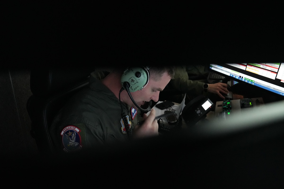 A man in a military uniform wearing headphones speaks into a speaker.