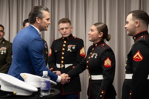 Secretary of War Pete Hegseth shakes hands with a Marine standing with other Marines in a room.
