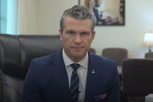 The secretary of war sits at a desk while speaking to a camera in an office.