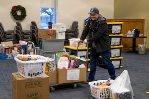 A man in a heavy winter coat pushes a flat bed cart with packages on it through a room full of Christmas packages