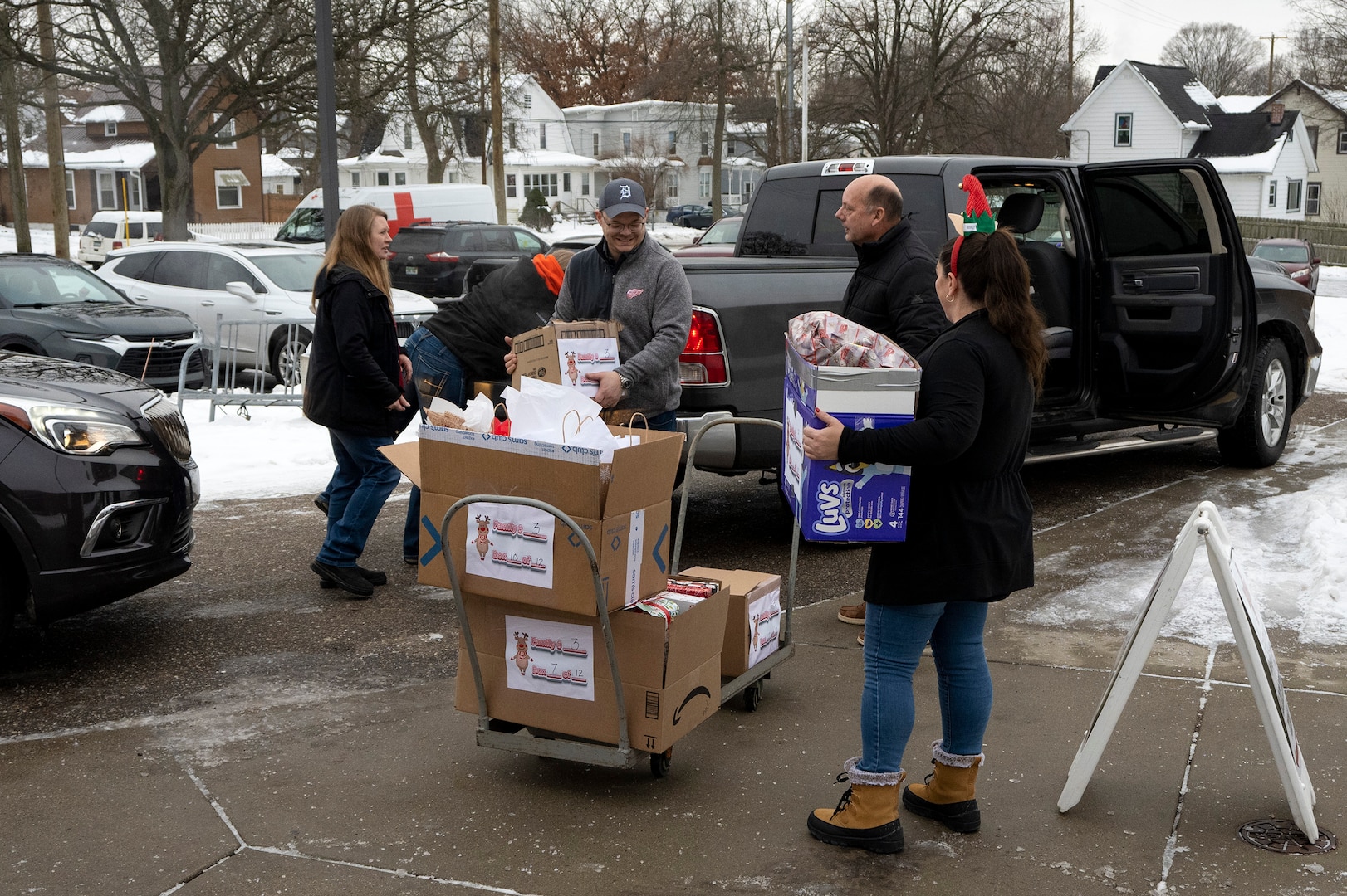 Five people a mix of men and women unload packages from a pickup truck onto a flat bed cart. there is snow on the ground.
