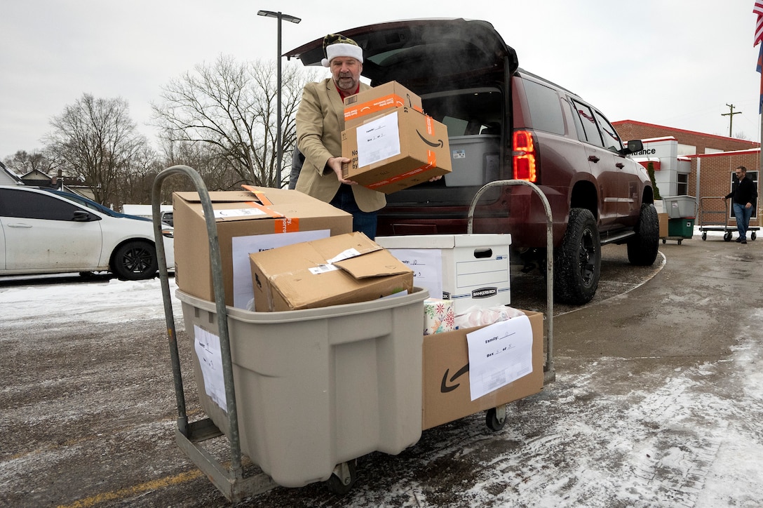 A man wearing a Santa hat removes packages from the back of a SUV outside and there is snow on the ground.