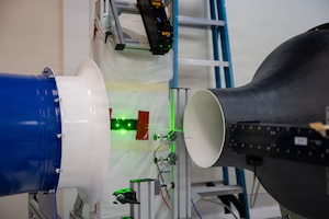 A wind tunnel system shows bright green laser lights between two tubes.