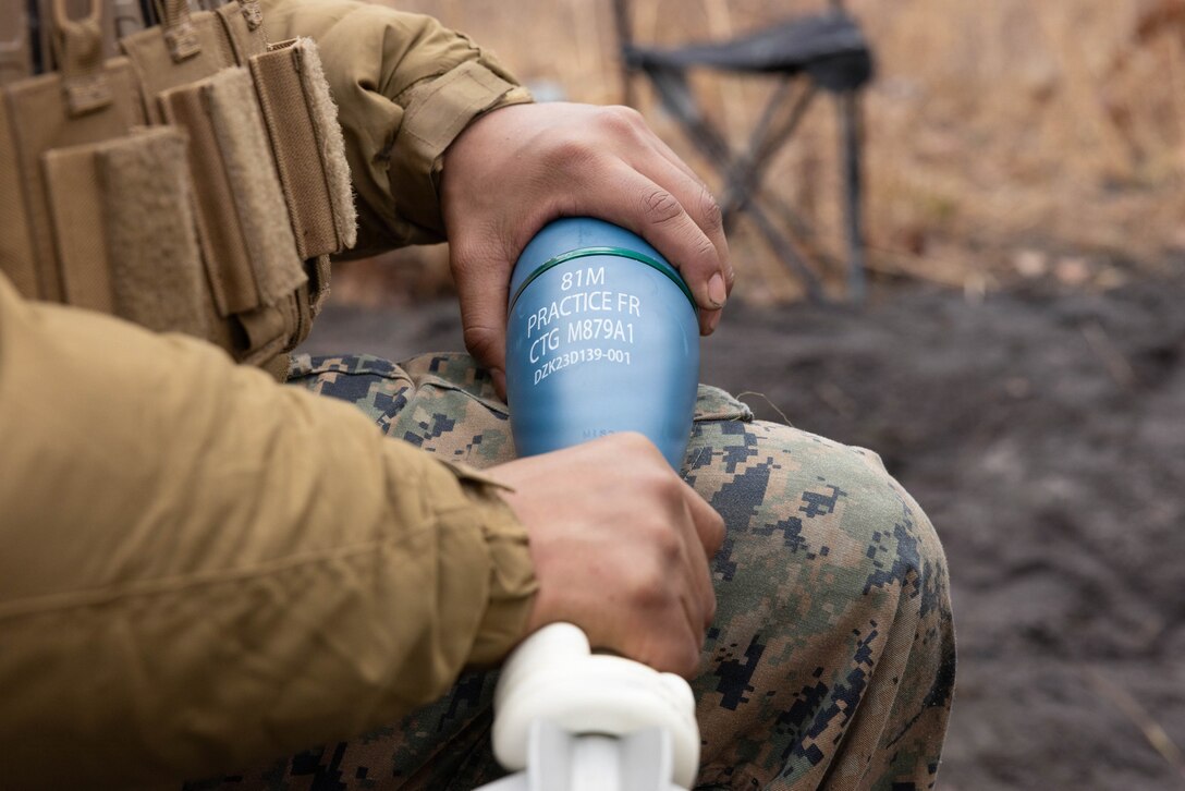A U.S. Marine Corps mortarman holds a practice round for an M252A2 81mm mortar system during a live-fire exercise at Joint Base McGuire-Dix-Lakehurst, New Jersey, Dec. 6, 2025. Marines with 2nd Battalion, 25th Marine Regiment, 4th Marine Division, participate in live-fire drills designed to improve tactical decision-making, leadership and technical skills while ensuring readiness for future missions. (U.S. Marine Corps photo by Lance Cpl. Breysson Villacortacampos
