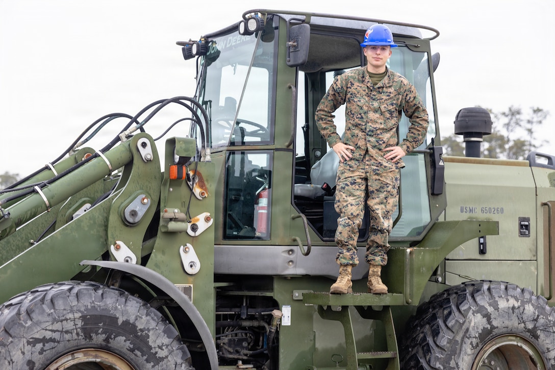 U.S. Marine Corps Lance Cpl. Jacob Black, a heavy equipment operator with II Marine Expeditionary Force Support Battalion, II MEF Information Group, poses with a Tractor, Rubber-Tired, Articulated Steering, Multi-Purpose vehicle at Marine Corps Base Camp Lejeune North Carolina, Dec. 5, 2025. Marines with II MEF Support Battalion then loaded the equipment in preparation for missions, honing their skills while showcasing the unit’s capabilities to prepare for onward movement at a moment’s notice. (U.S. Marine Corps photo by Lance Cpl. Dorian Melrath)