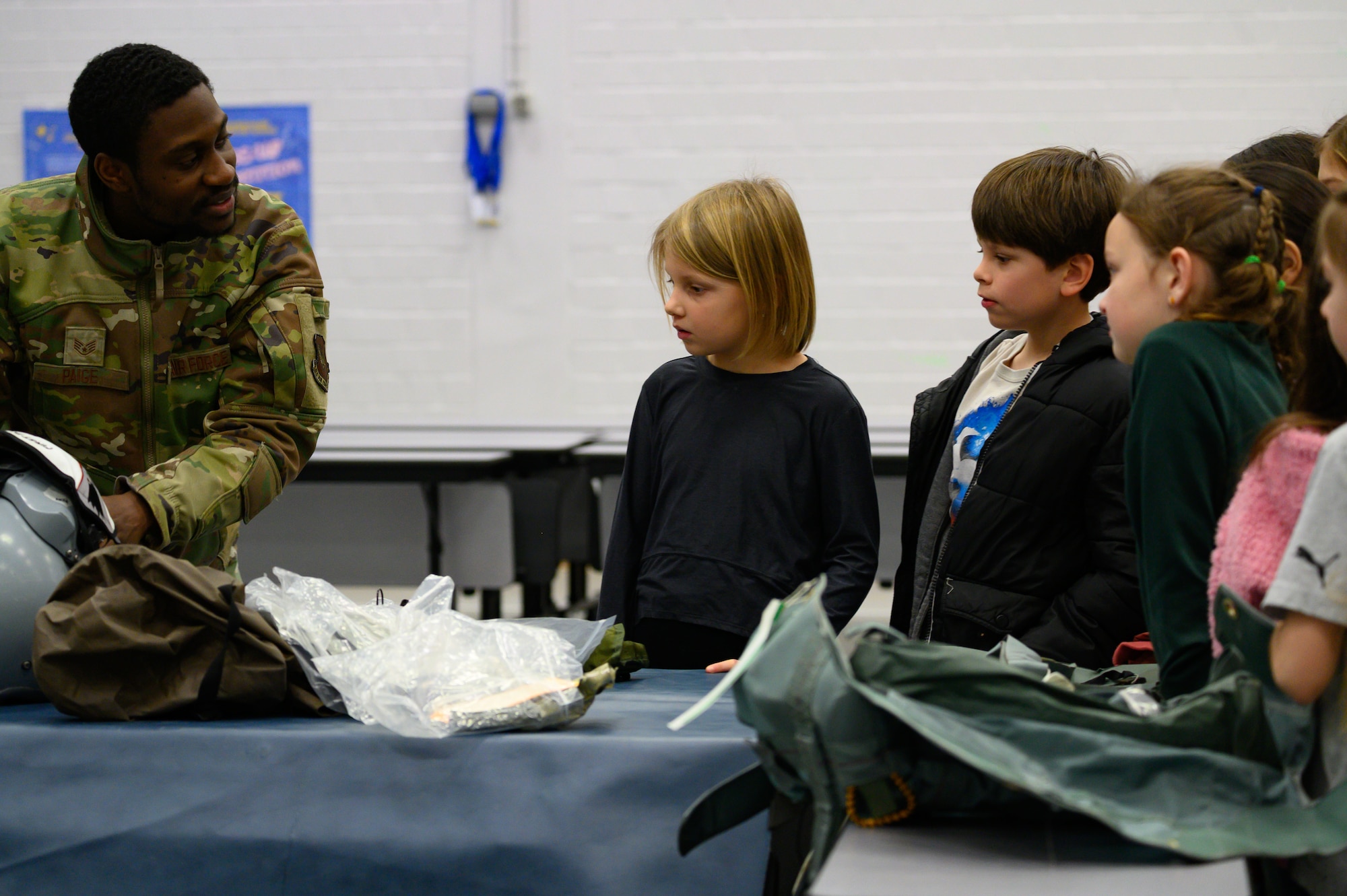 An Airman holds a parachute while explaining its use to a group of third grade students.