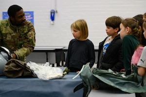 An Airman holds a parachute while explaining its use to a group of third grade students.